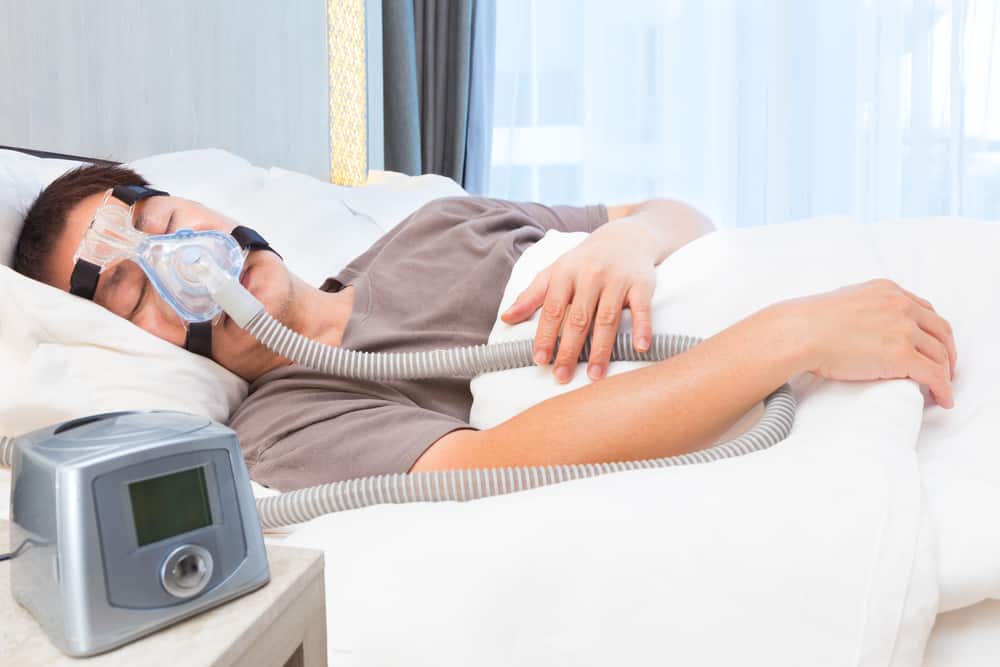 middle age asian man sleeping in his bed wearing CPAP mask connecting to air hose and CPAP machine, device for people with sleep apnea